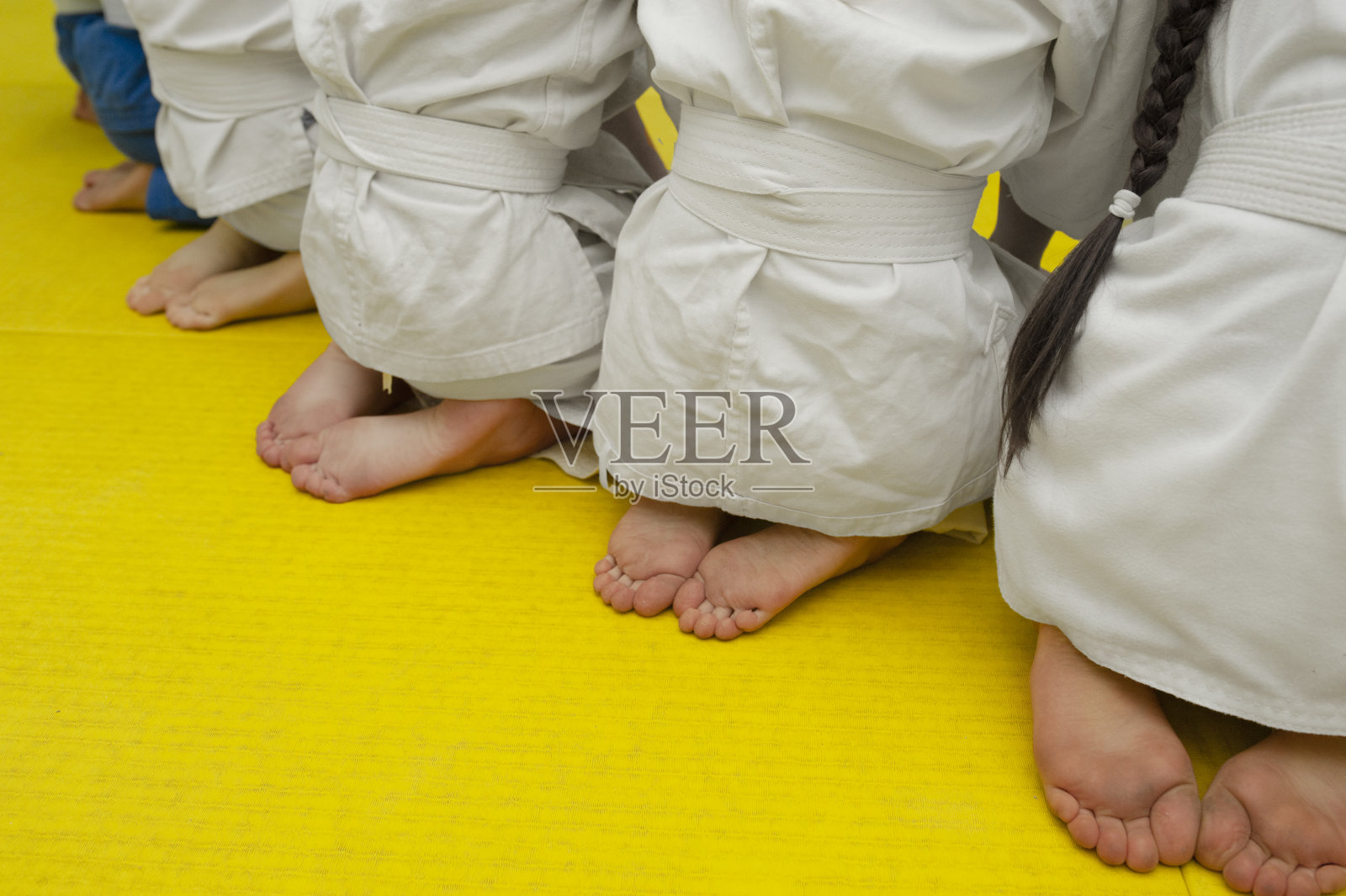 穿着白色运动服的孩子们赤裸着双腿和脚后跟,系着摔跤腰带躺在黄色床垫上照片摄影图片
