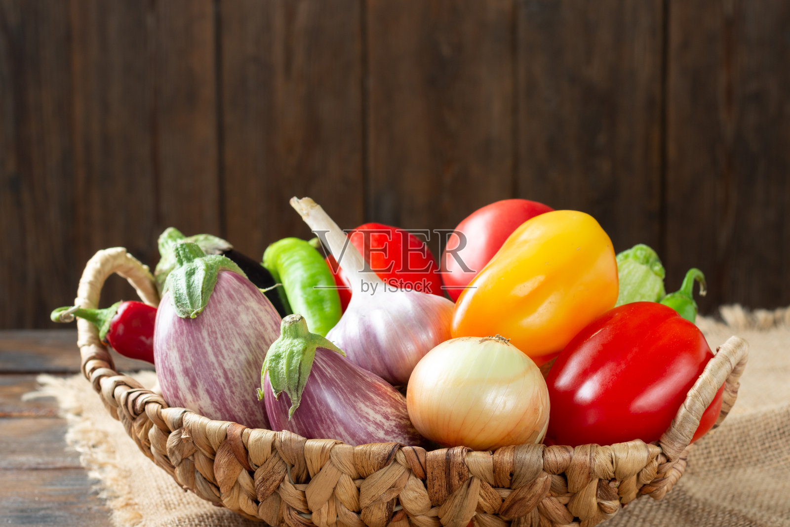 桌子上的篮子里装着各种各样的蔬菜。篮子里有很多不同的生蔬菜。桌上放茄子、西红柿、大蒜、甜椒、洋葱。健康饮食的概念照片摄影图片
