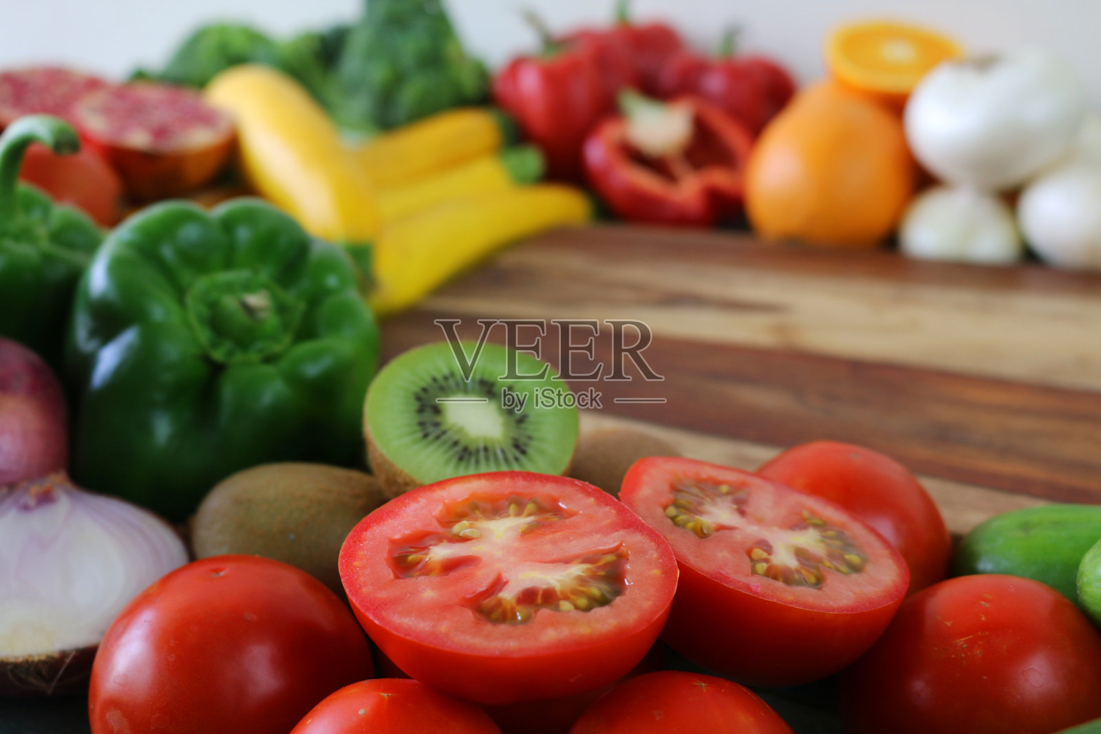 一组完整的和对半的水果和蔬菜放在木砧板上的图片,猕猴桃,青椒,番茄,西葫芦,红洋葱,橙子,石榴和红辣椒,重点放在前景照片摄影图片