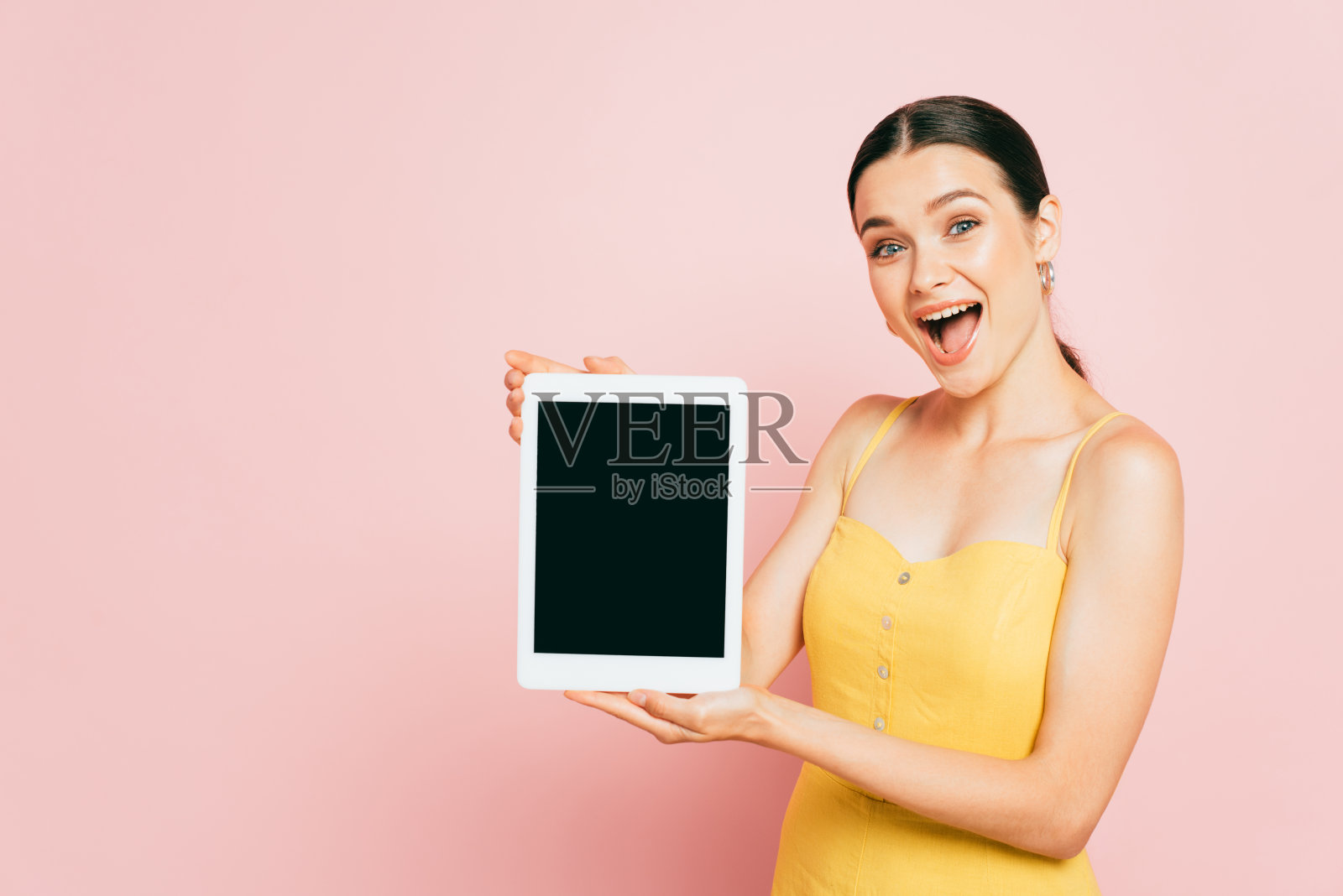 兴奋的褐发年轻女子展示了一个粉红色空白屏幕的数字平板电脑照片摄影图片