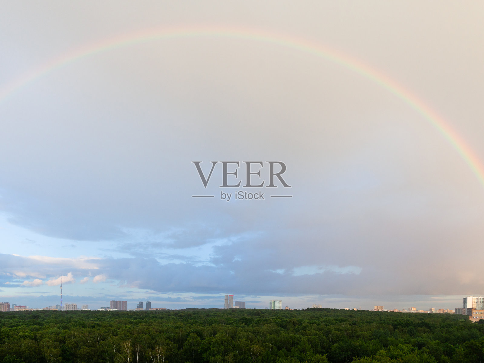 蓝色多云的天空中,森林和房屋上空出现彩虹照片摄影图片