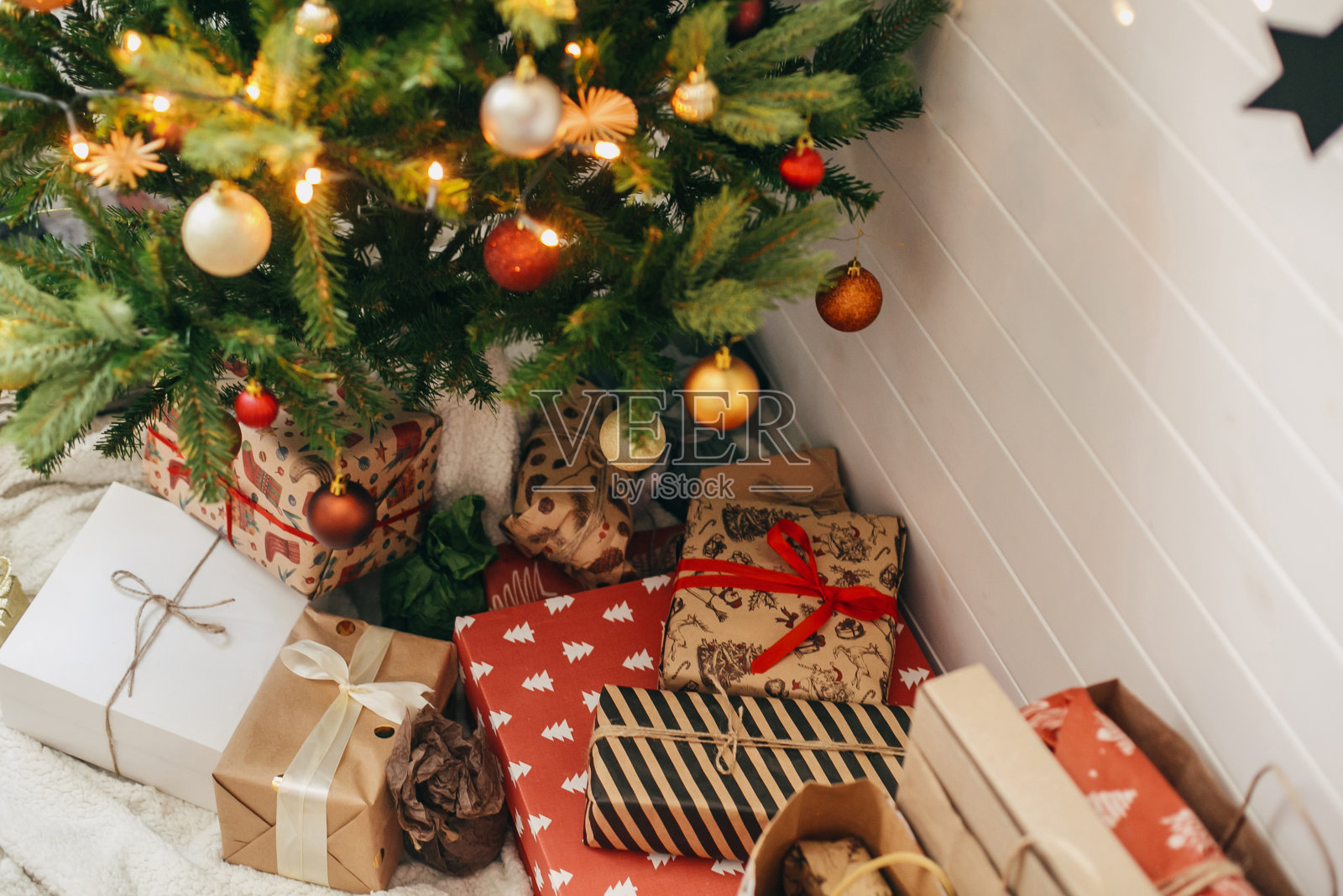 圣诞快乐。圣诞树下时尚的圣诞礼物。礼盒包装在工艺现代纸和装饰树与红色和金色的小玩意在喜庆的斯堪的纳维亚房间。照片摄影图片