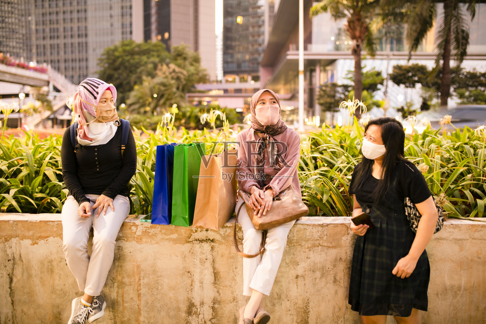 2019冠状病毒病大流行期间,亚洲女性戴着口罩坐在公园里照片摄影图片