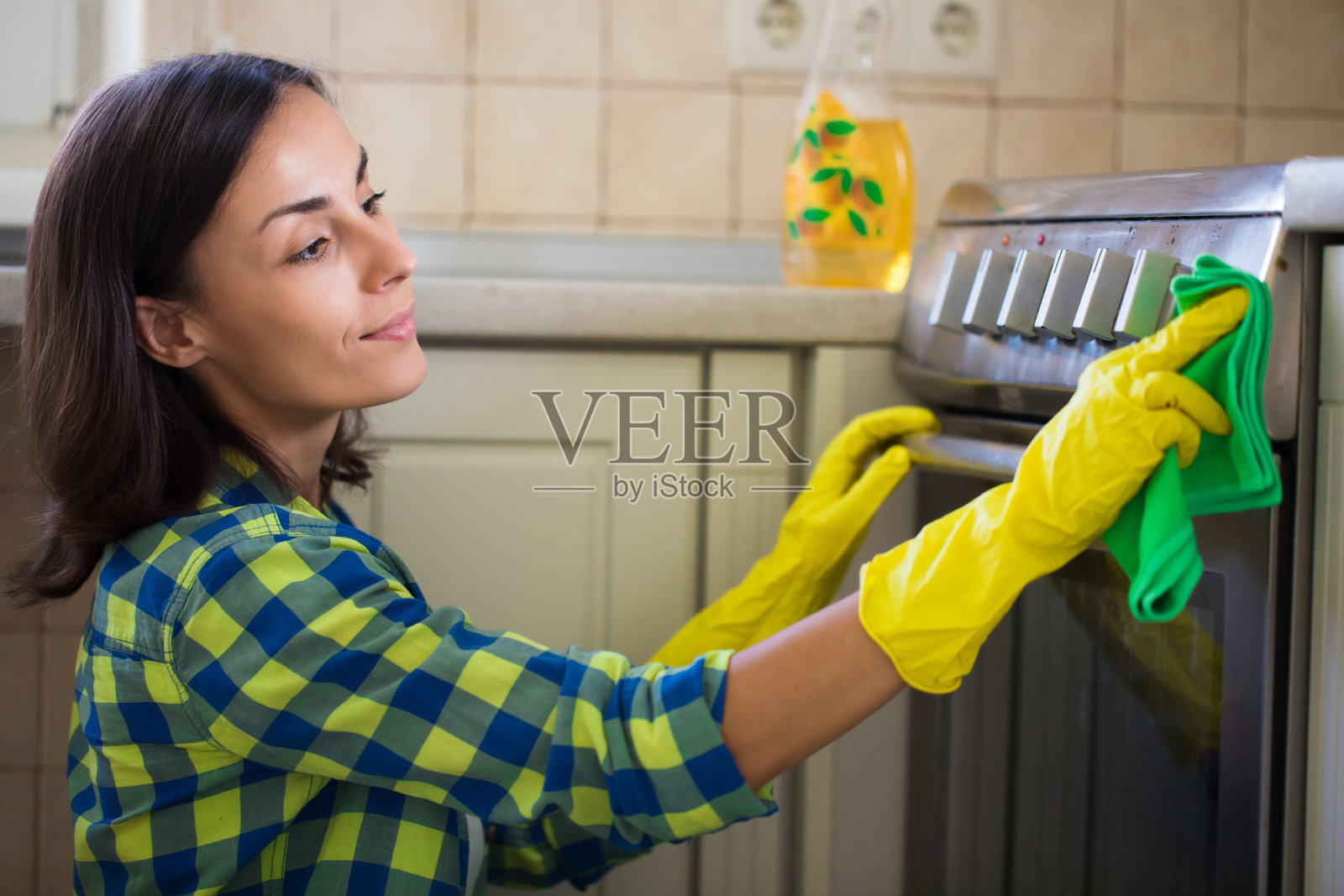 一位穿着休闲装的漂亮年轻女子在打扫房子的时候,正在擦拭厨房里的电炉。照片摄影图片