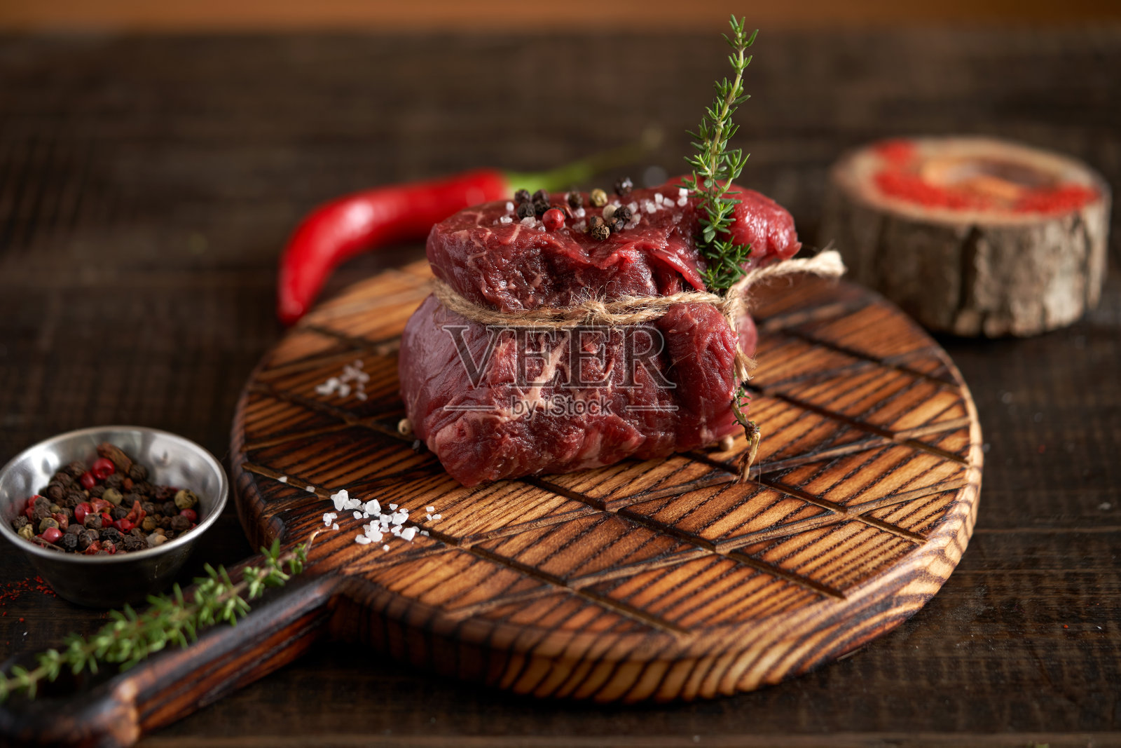 新鲜、多汁、陈年的菲力牛排用麻绳绑在砧板上,配上调味料——豌豆、番茄干、红辣椒、红辣椒放在木板上。顶部视图,放置文本照片摄影图片