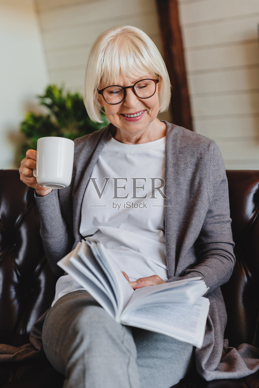 垂直肖像的微笑成熟的女人读书,而放松在沙发上在家与一杯咖啡照片摄影图片