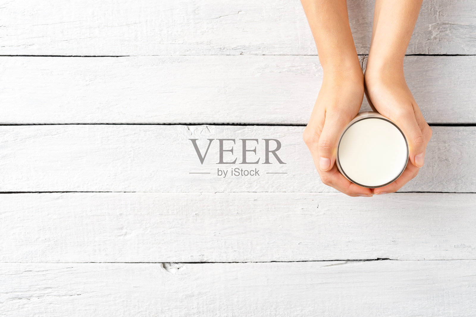 女人的手拿着牛奶杯在白色的木桌与copyspace。俯视图照片摄影图片