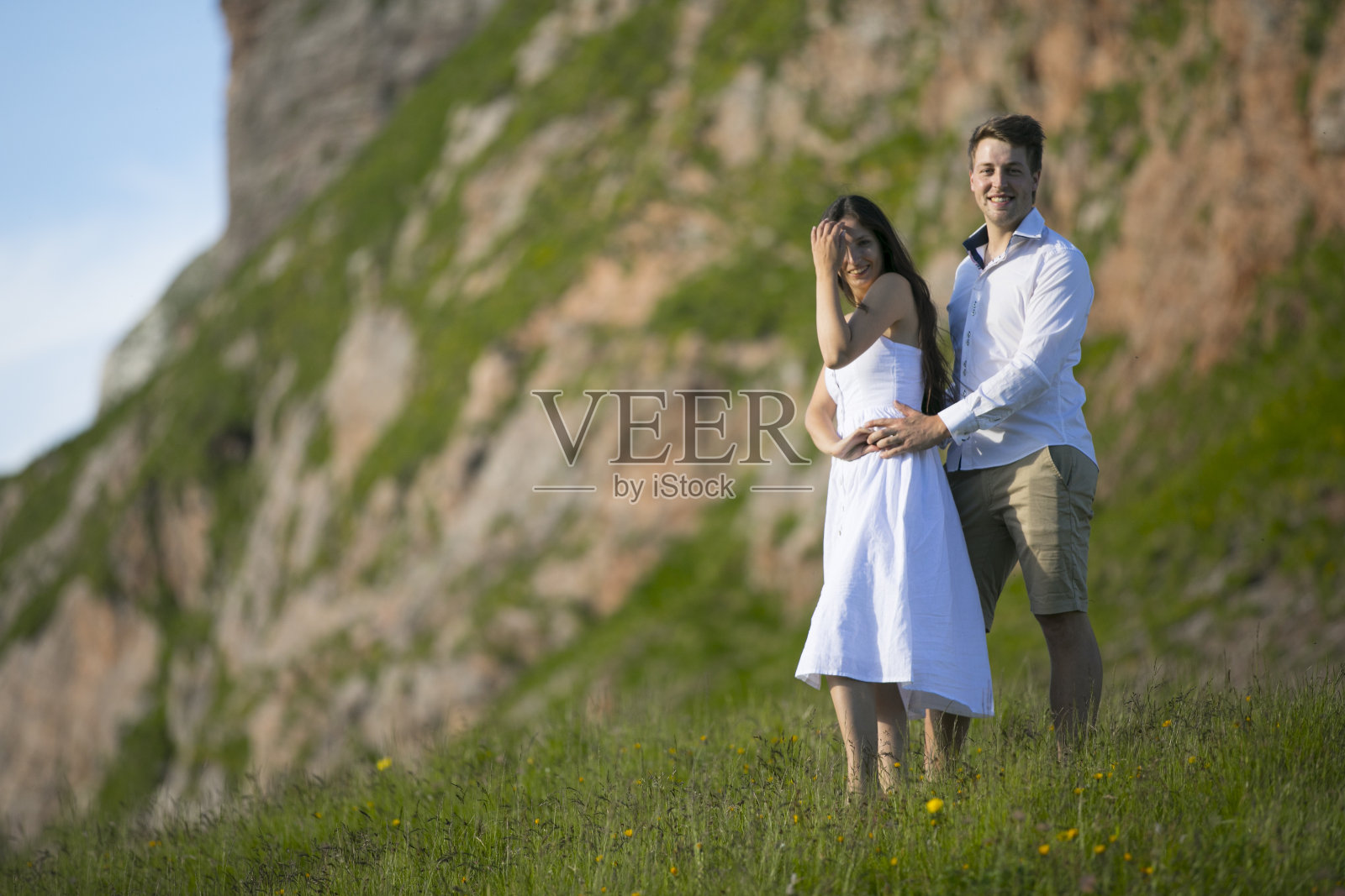 微笑的年轻成年夫妇站在山上的草地上看镜头照片摄影图片