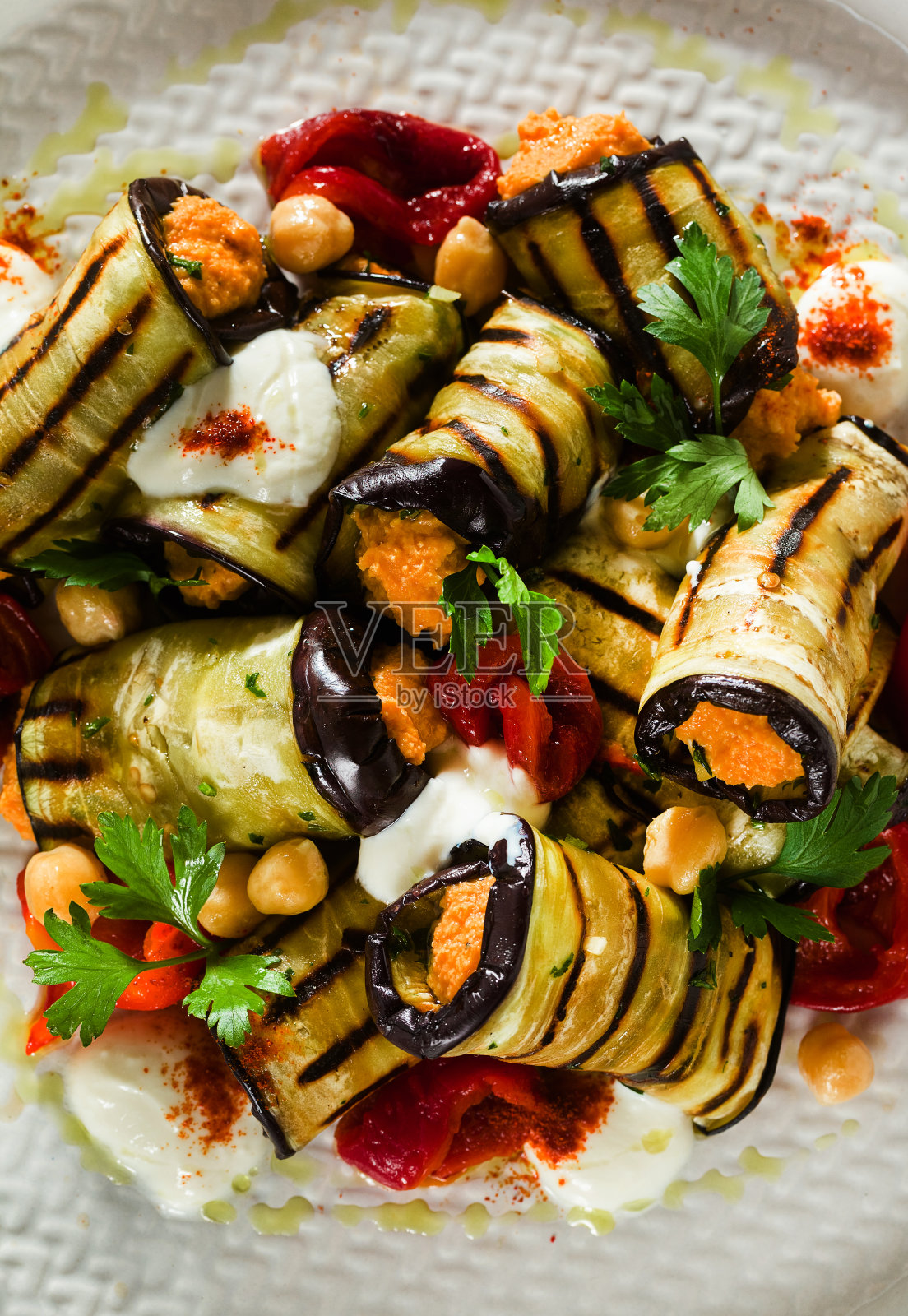 桌上有烤茄子卷、红甜椒、鹰嘴豆泥和辣酸奶。美味的素食食谱照片摄影图片