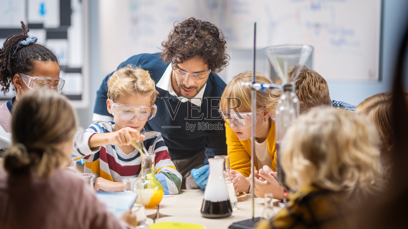 小学科学课堂:热情的老师向不同的孩子讲解化学,小男孩在烧杯里混合化学物质。孩子有兴趣学习照片摄影图片