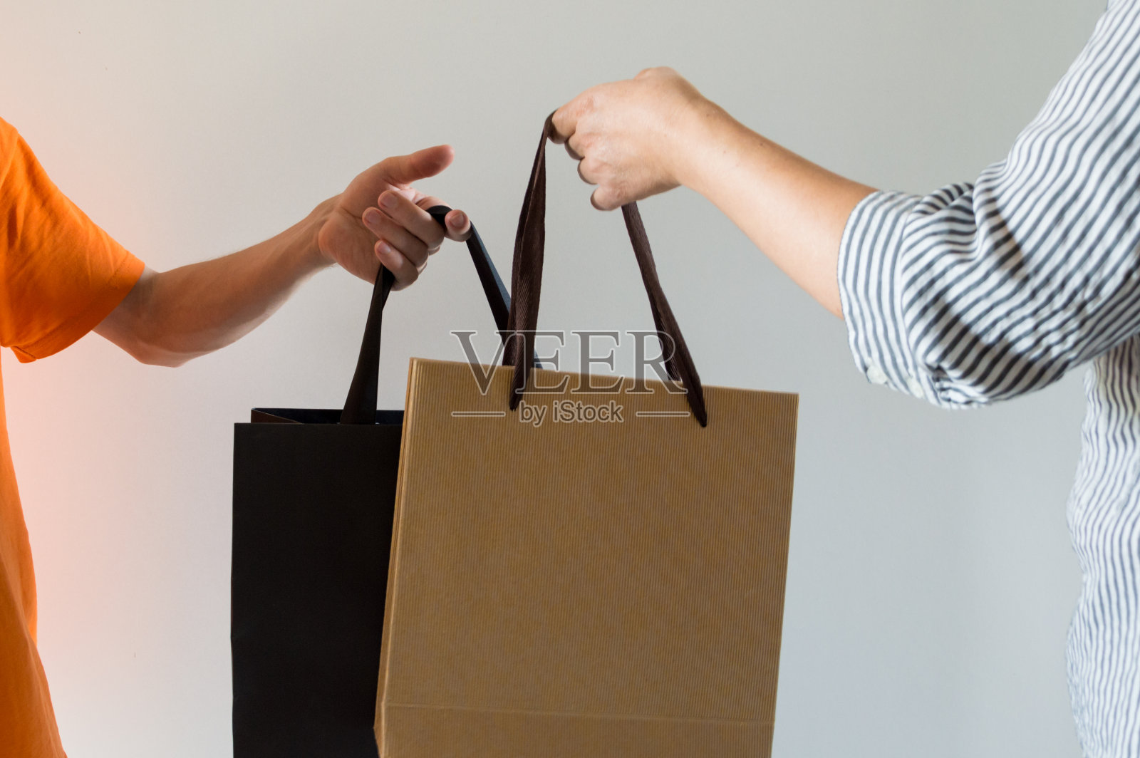 一个拿黑包的年轻男子的手和一个拿轻购物袋的女人的手。照片摄影图片