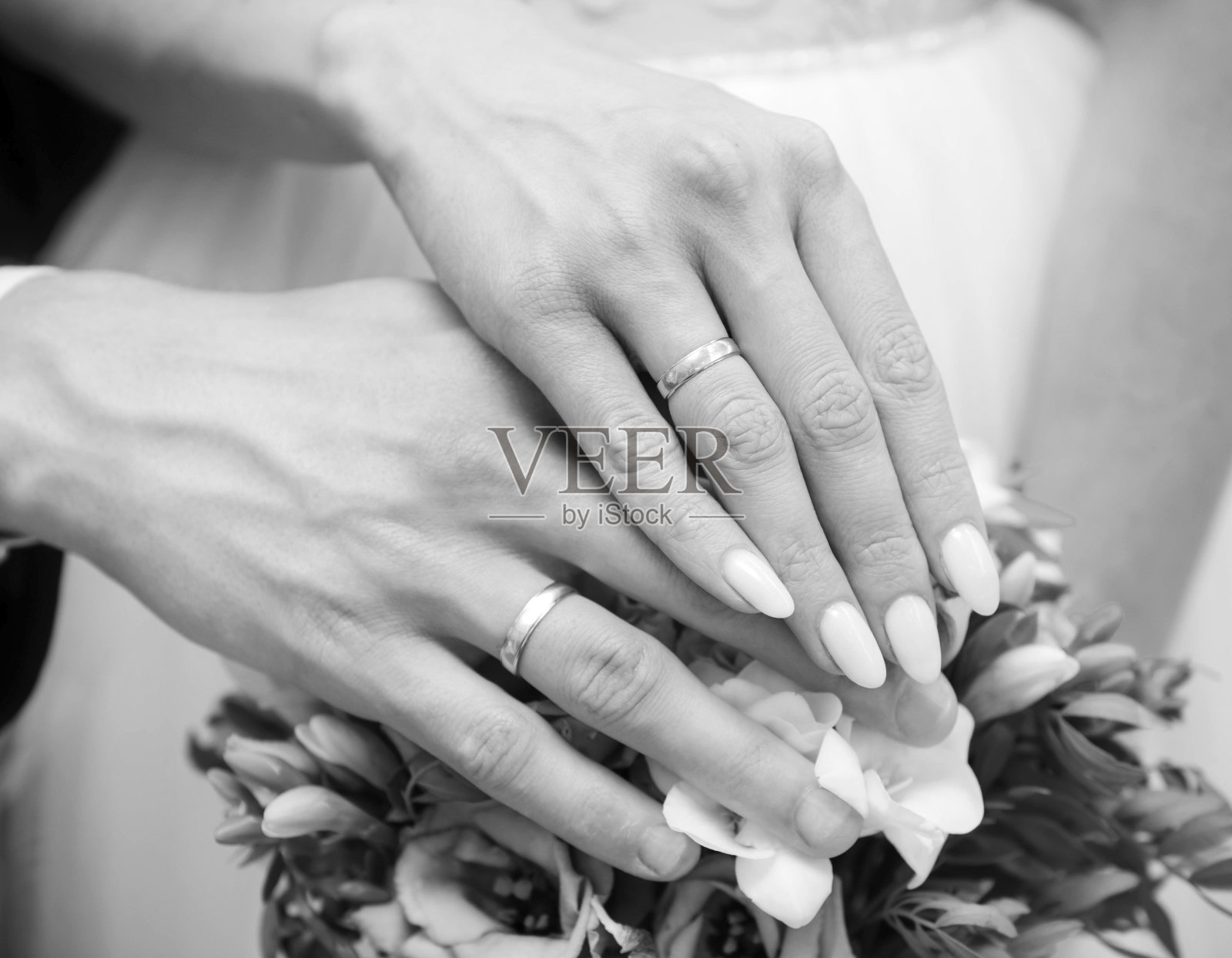 新郎和新娘的手与金结婚戒指在一个花束的背景,新婚夫妇,黑色和白色照片摄影图片
