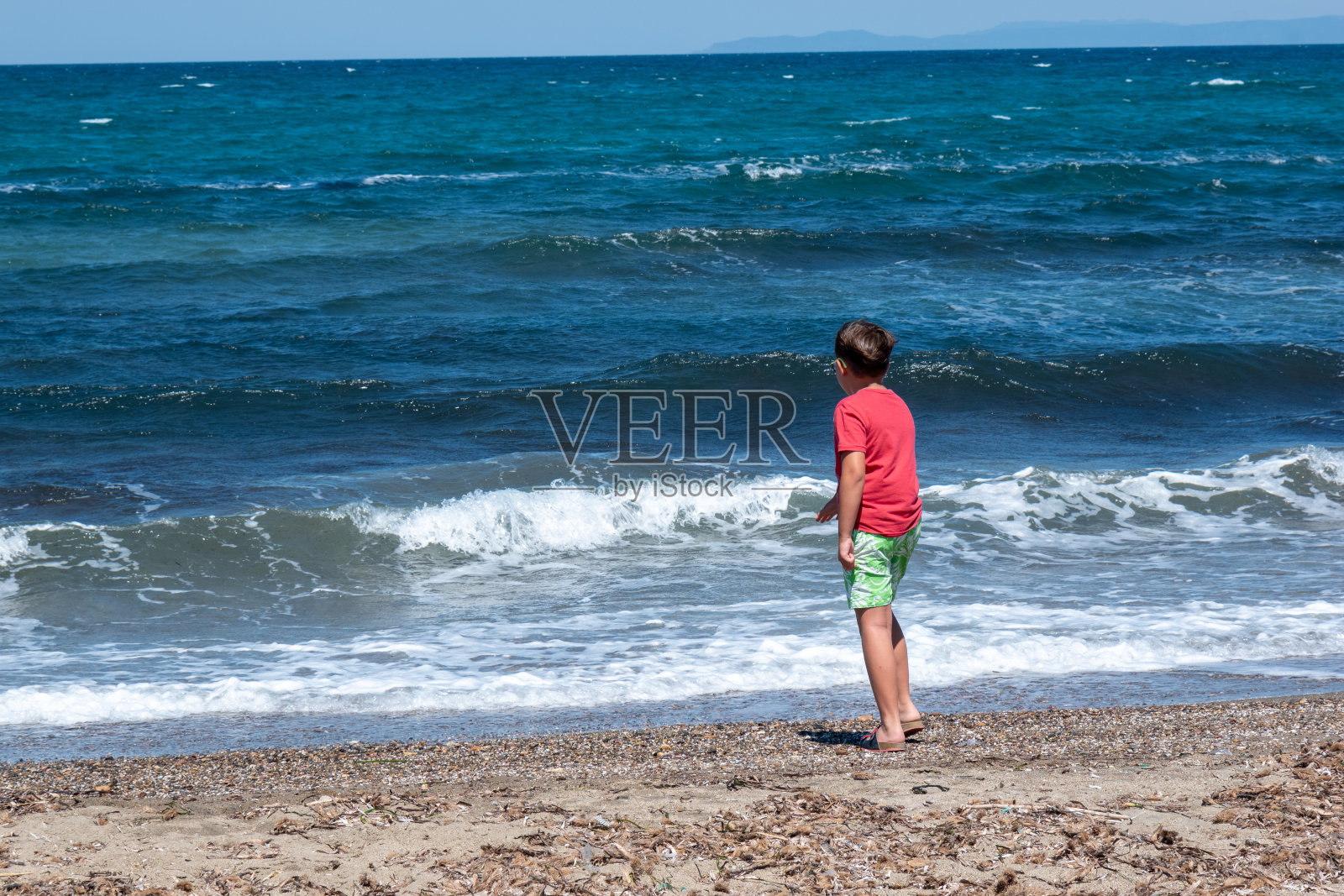 一个10岁的男孩看着汹涌的大海。照片摄影图片