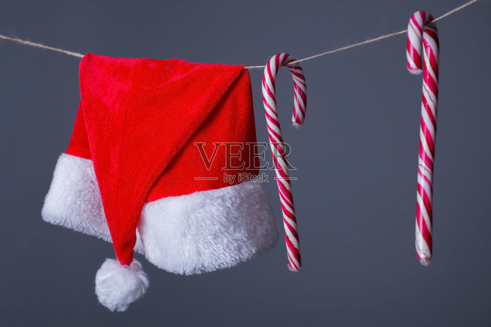 圣诞老人帽子的特写,还有挂在晾衣绳上的新年糖果。在一个灰色的背景。新年结束的背景。厌倦了圣诞节假期照片摄影图片
