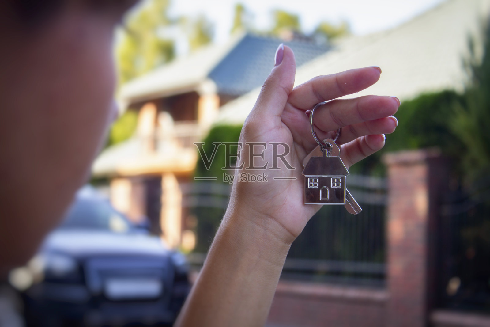 一个女人手里拿着房子的钥匙,背景是住宅楼和汽车。买房和租房的概念。照片摄影图片