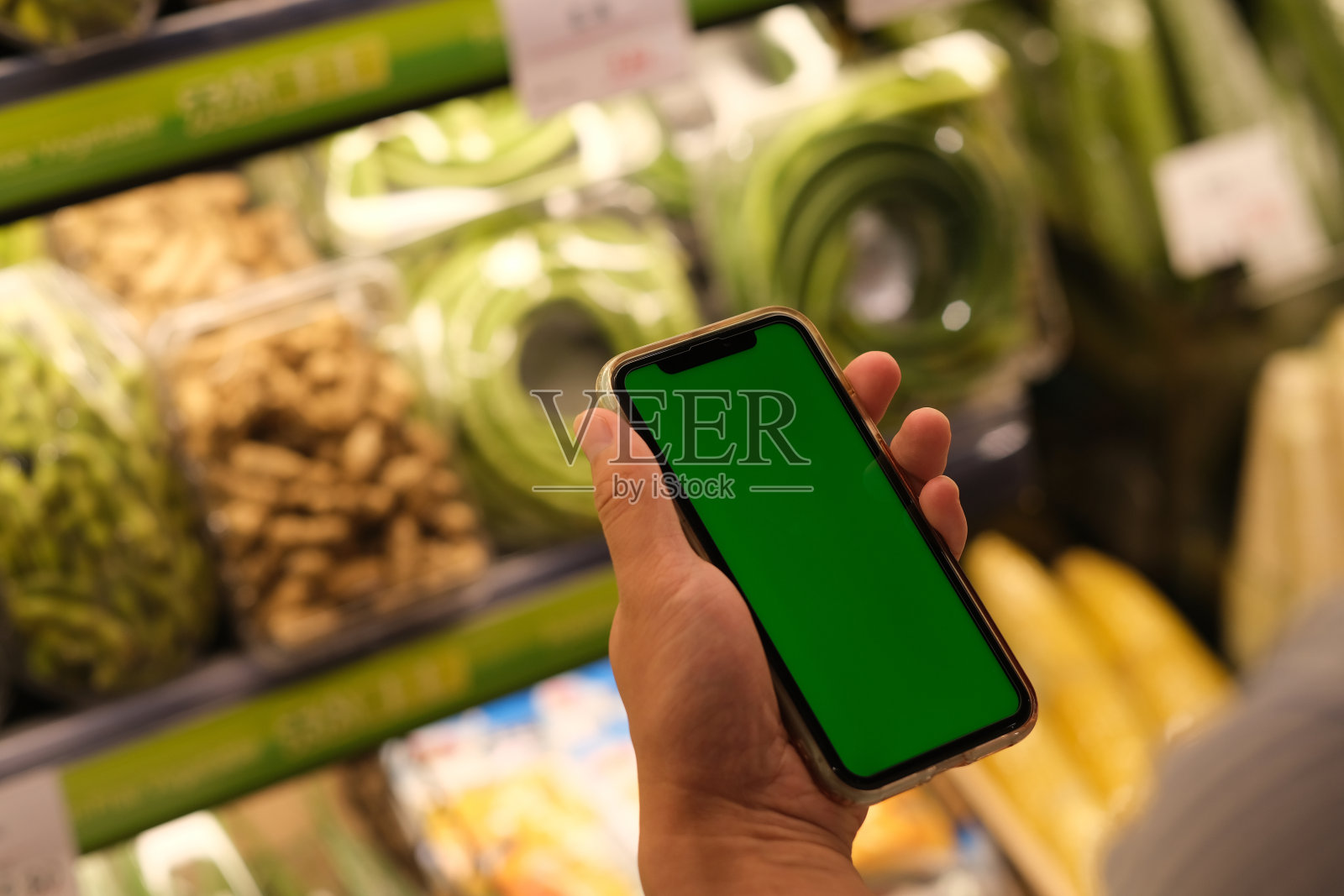 在杂货店拿着绿色屏幕智能手机的人的肩膀上照片摄影图片