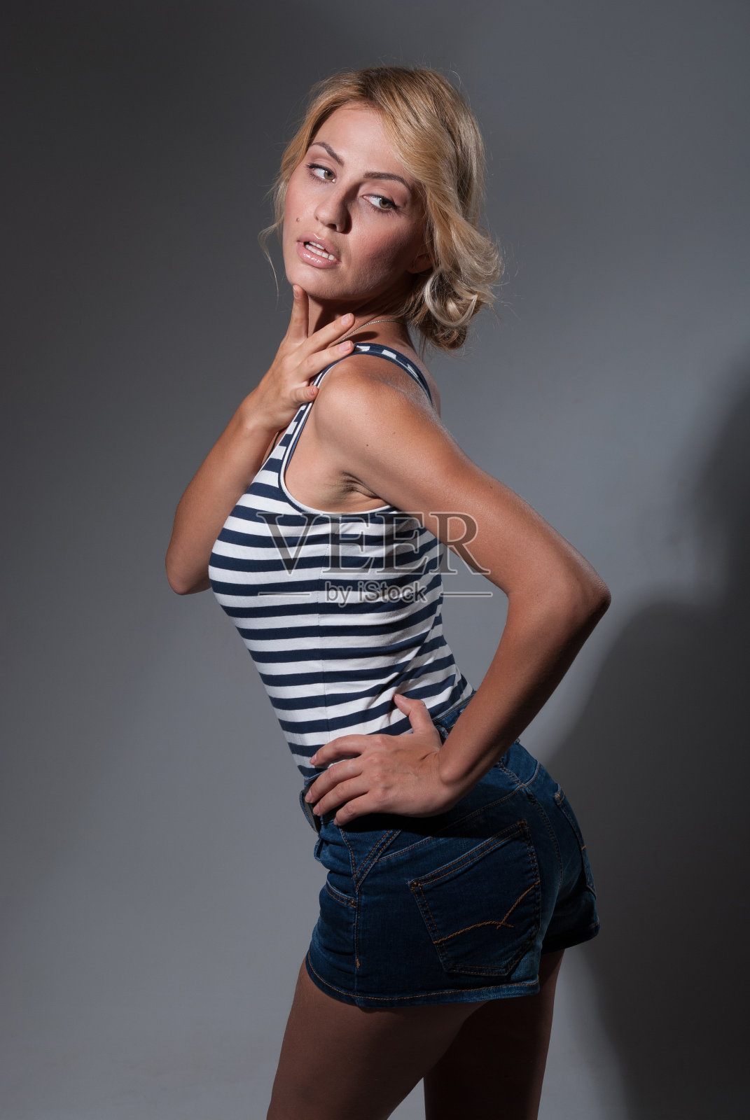 一个美丽的年轻女孩的肖像在条纹t恤和牛仔裤短裤孤立在灰色照片摄影图片