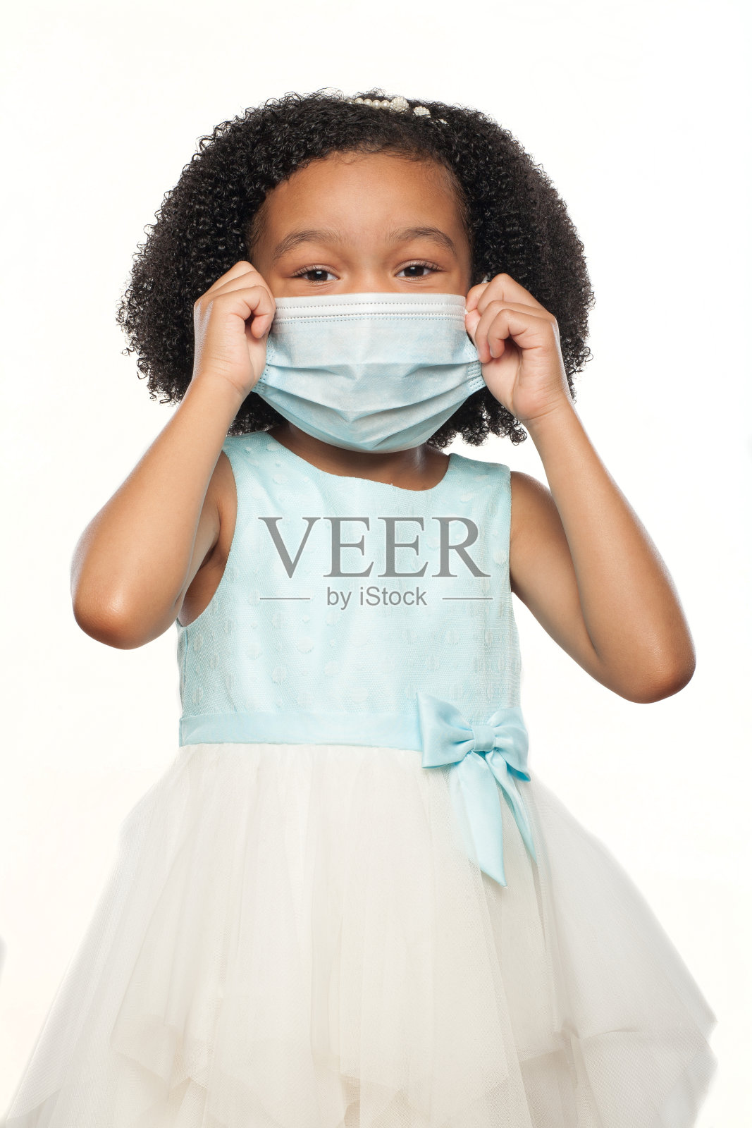 可爱的非洲裔美国年轻女孩戴着一个外科口罩与可爱的面部表情照片摄影图片