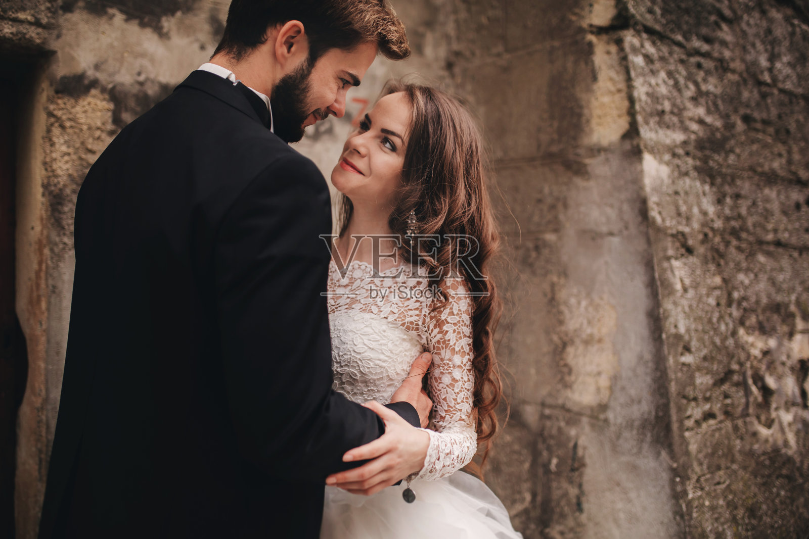 幸福的新婚夫妇拥抱和亲吻在古老的欧洲城镇街道,美丽的新娘在白色婚纱与英俊的新郎在一起。结婚的那一天。照片摄影图片