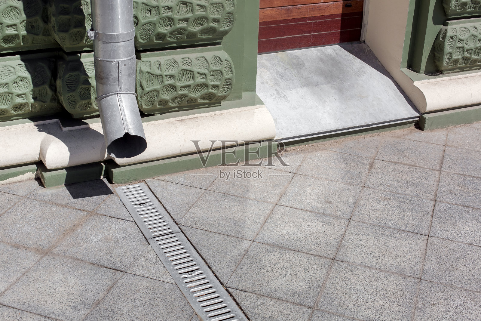 城市工程结构落水管上的绿色立面建筑与排水格栅的灰色石材花岗岩人行道用方形瓷砖复制空间,特写城市基础设施的细节,无人。照片摄影图片