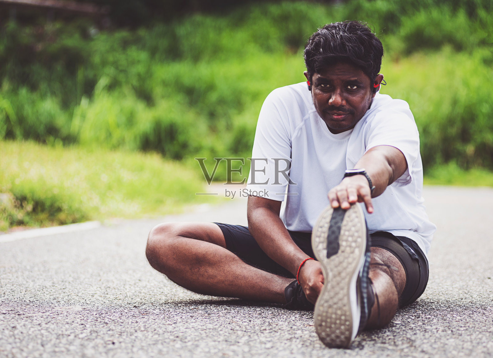 黑人运动员戴着手表,他坐着拉脚趾伸直双腿和膝盖照片摄影图片