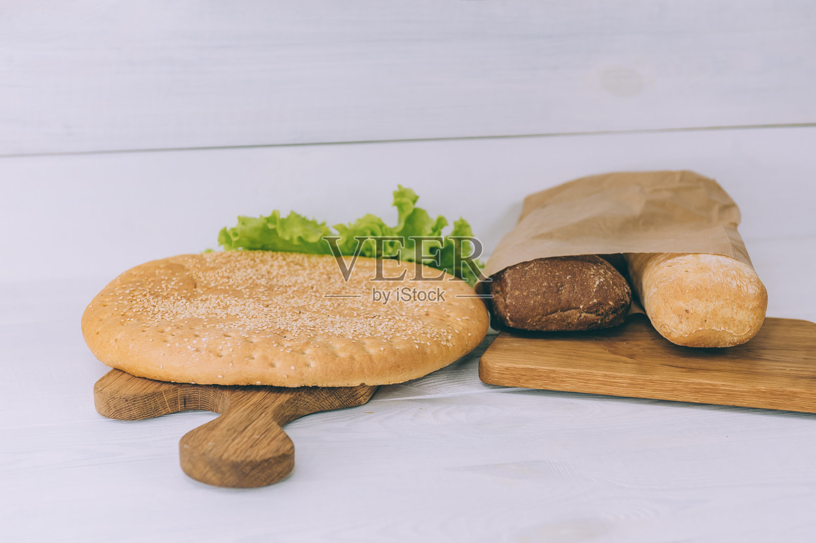 白色桌子上的切菜板上的带香草的法棍面包颗粒。照片摄影图片