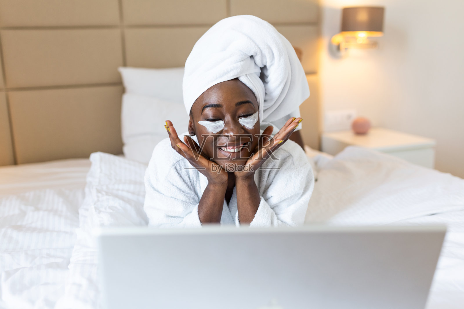 一名年轻女子在卧室使用笔记本电脑时将眼罩涂在脸上的肖像。年轻女性在家工作的生活方式概念。照片摄影图片