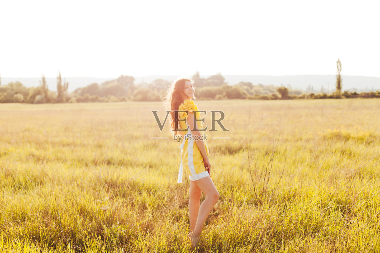 一个美丽的女人的肖像,穿着黄色的衣服在一个日落的田野照片摄影图片