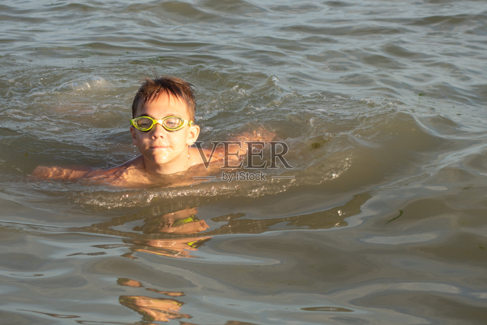 一个10岁的男孩在一个阳光明媚的日子里在海里游泳。照片摄影图片