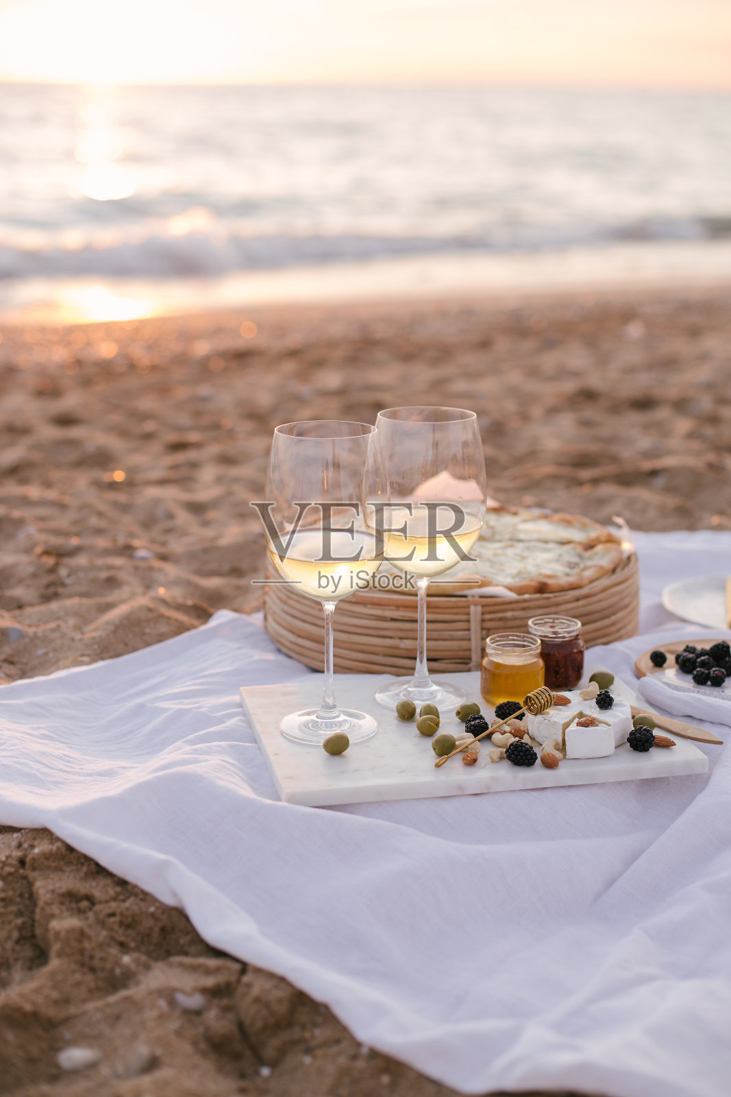 夏日野餐在日落的海滩上,白葡萄酒,比萨饼,奶酪,橄榄和新鲜的水果。照片摄影图片