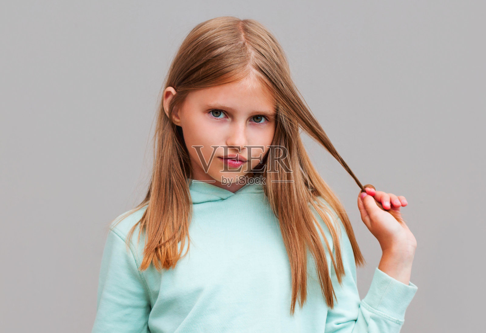 年轻美丽可爱开朗的女孩的肖像看着相机在灰色的背景触摸她的头发照片摄影图片