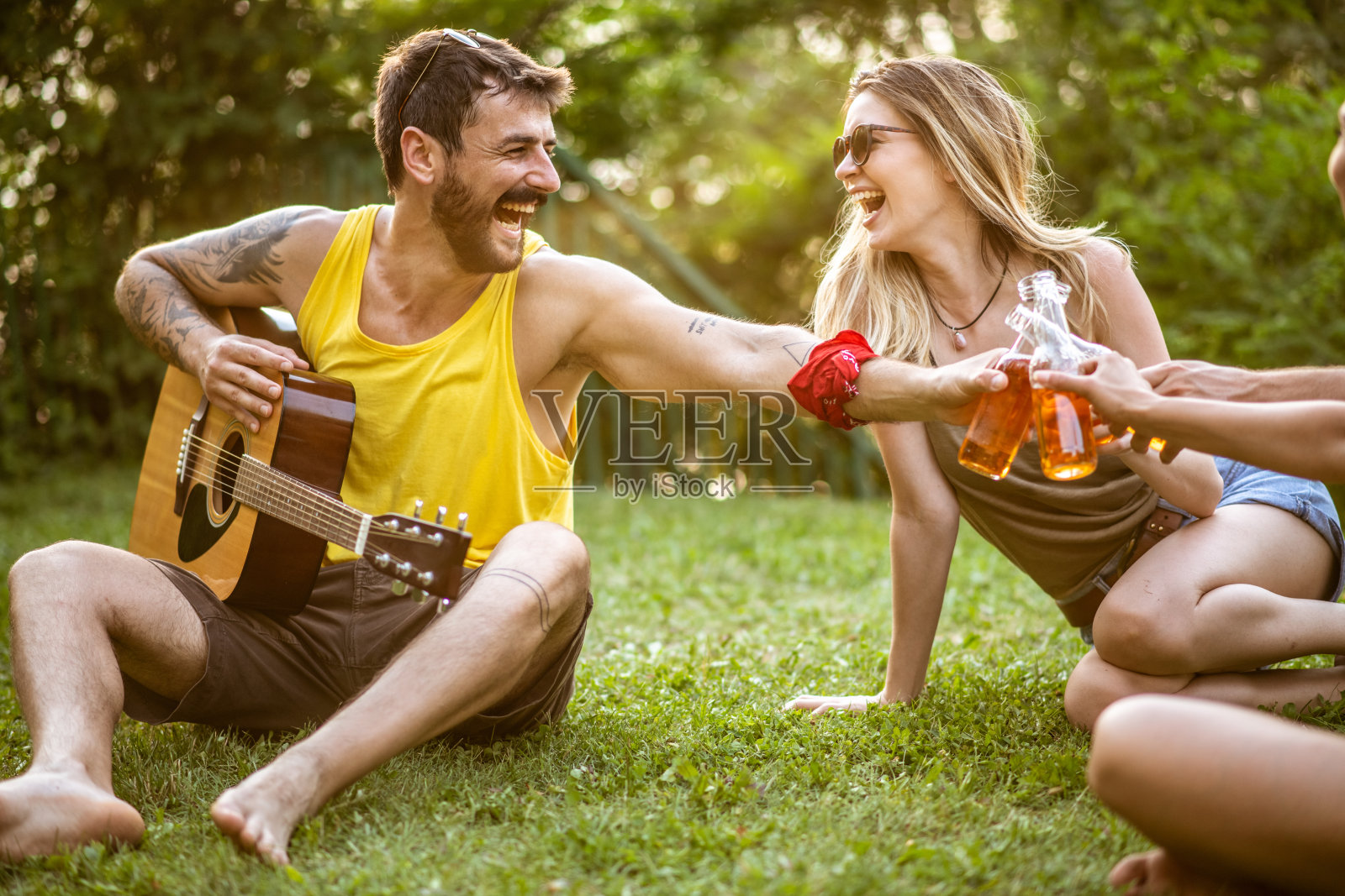 年轻人坐在花园里,喝着啤酒,其中一个拿着一把原声吉他照片摄影图片