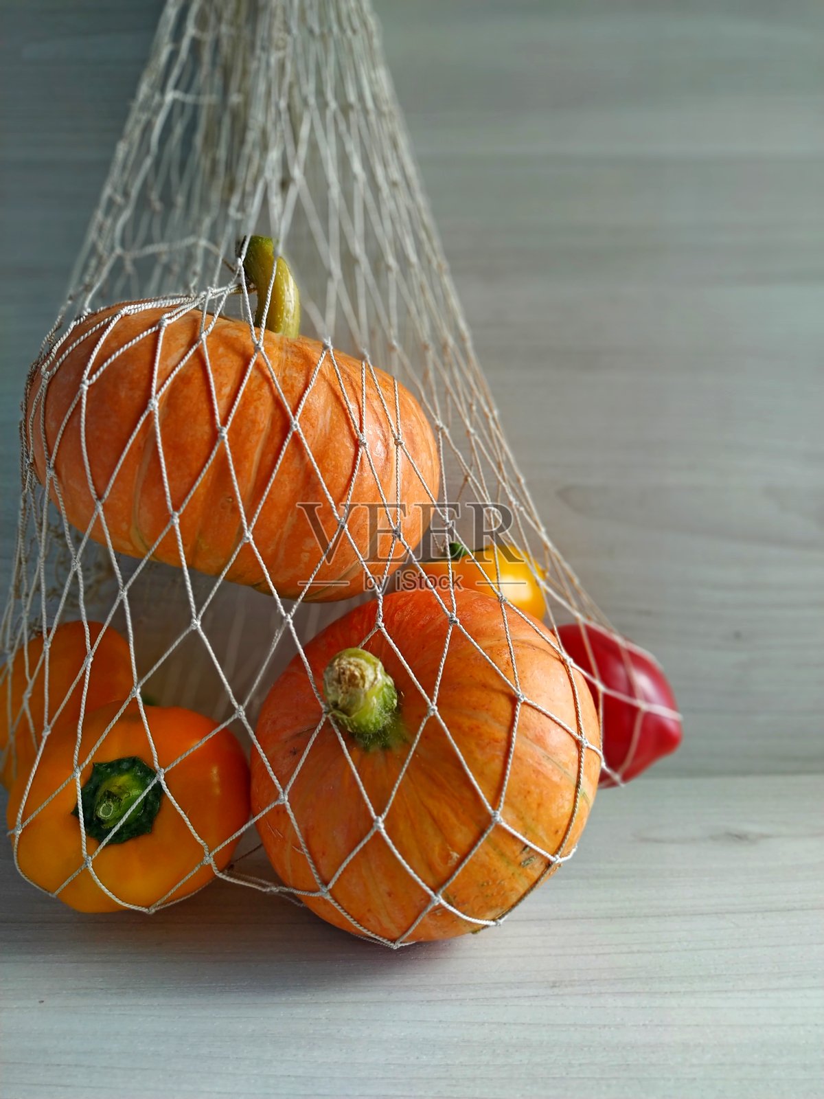 收获时间。南瓜和辣椒放在一个网袋里,背景是浅色的木头照片摄影图片