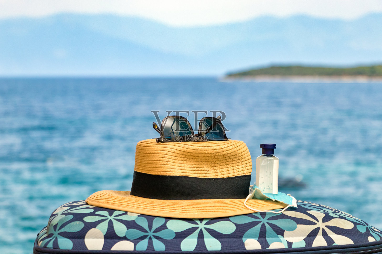 一顶草帽、口罩、洗手液和太阳镜放在沙滩的背景上。照片摄影图片