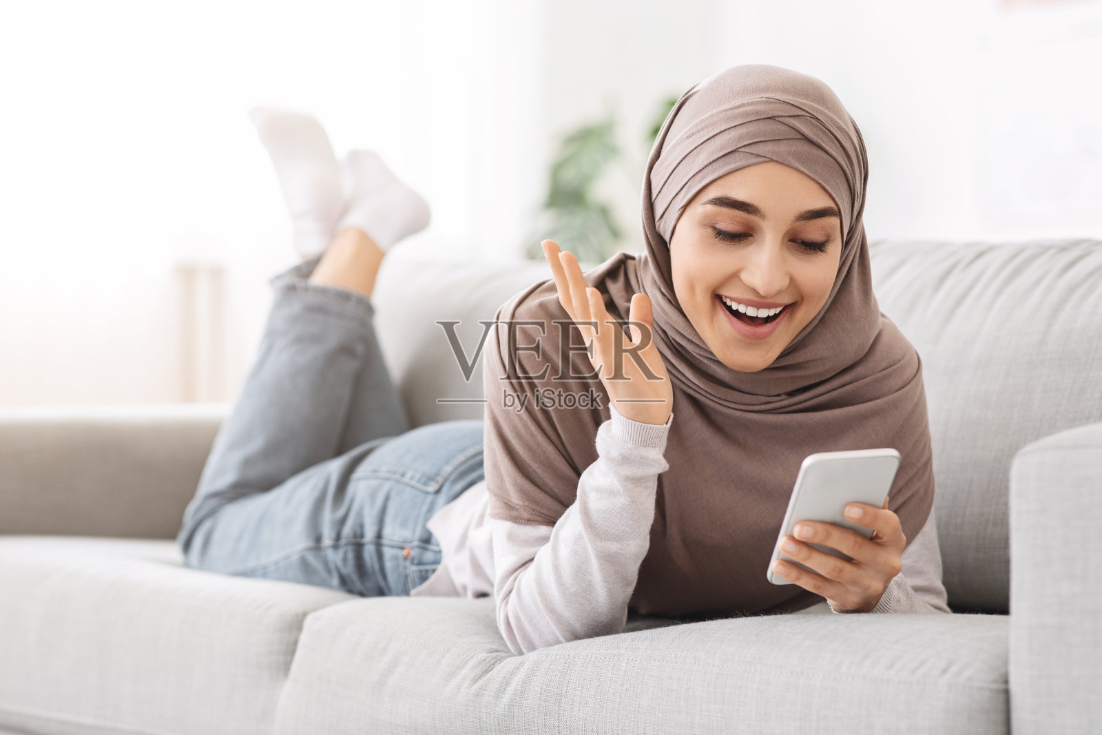 好消息。兴奋的阿拉伯女孩躺在沙发上用智能手机,阅读信息照片摄影图片