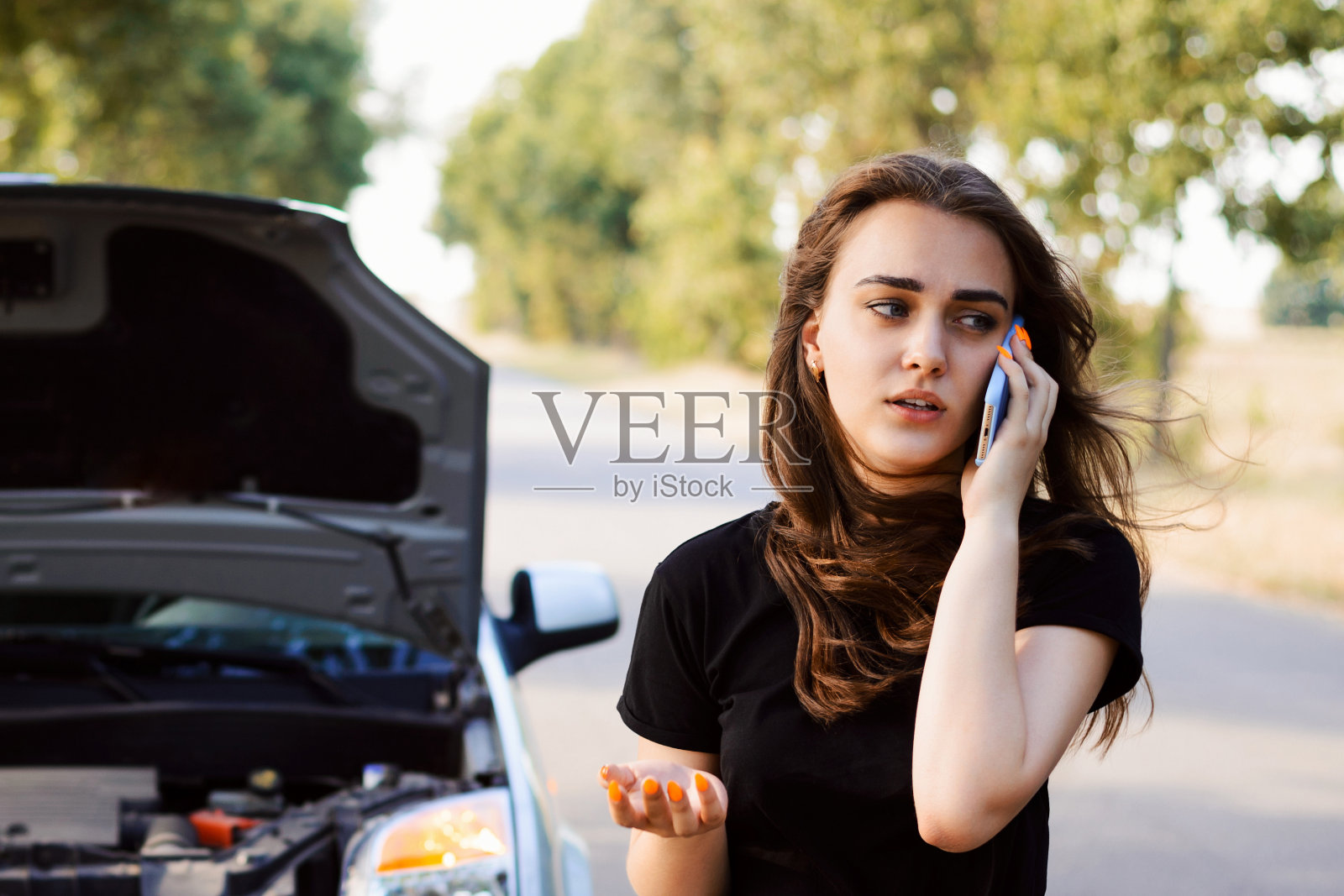 一辆车在柏油路边抛锚了,年轻的学生司机打电话叫救援队来帮助她并修理汽车照片摄影图片