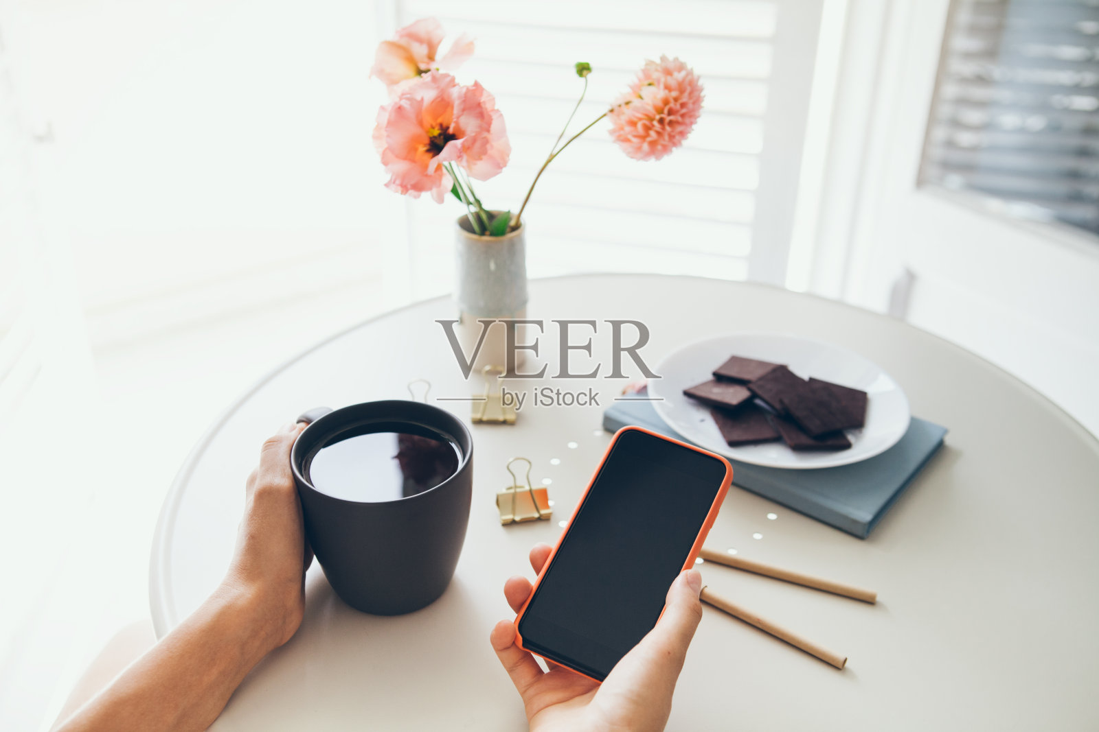 近距离的女人拿着一杯茶和手机,阅读新闻,社交网络,上网而呆在家里。照片摄影图片