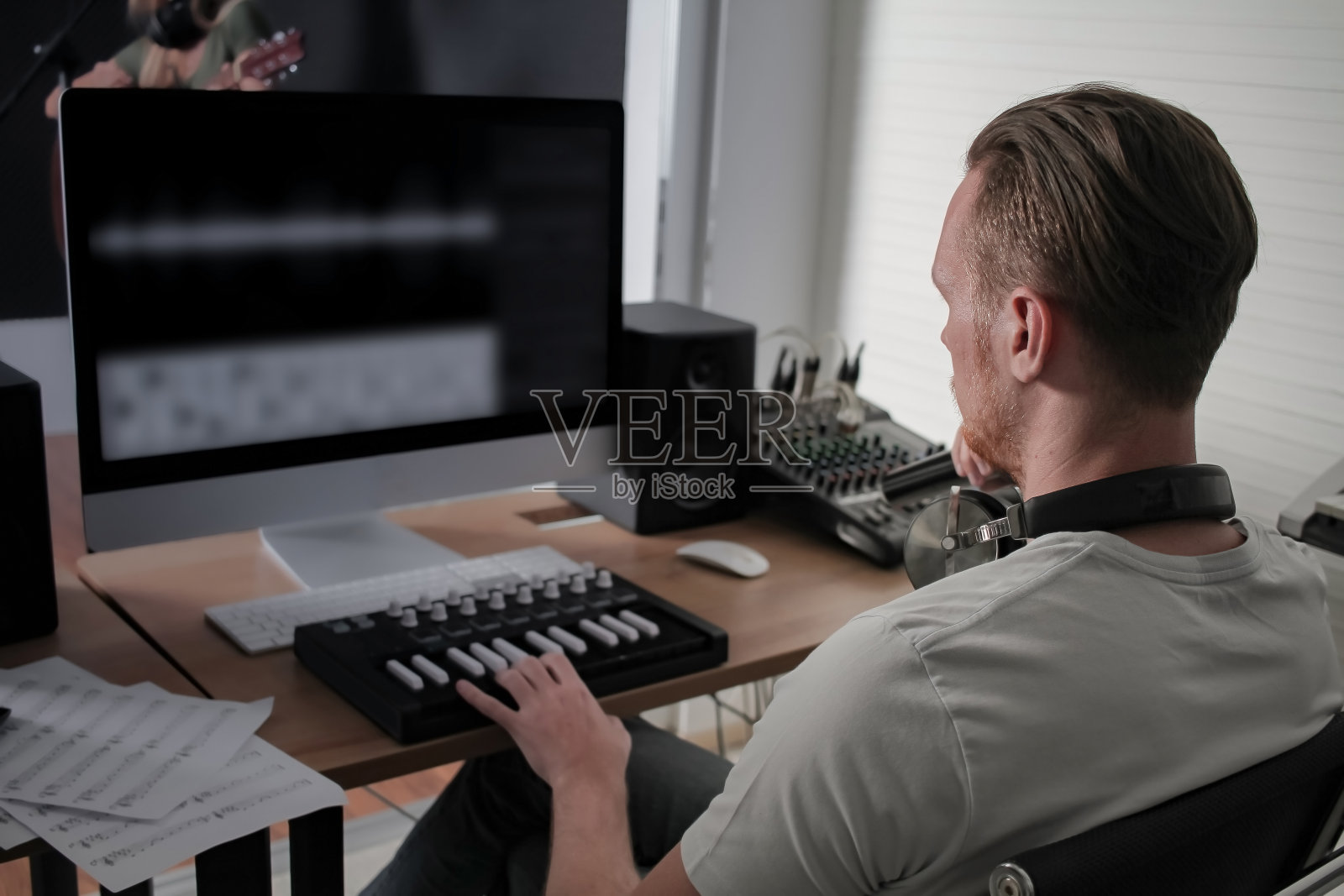 年轻的白人男性音乐作曲家打midi键盘为安排歌曲在家庭工作室电脑上。照片摄影图片