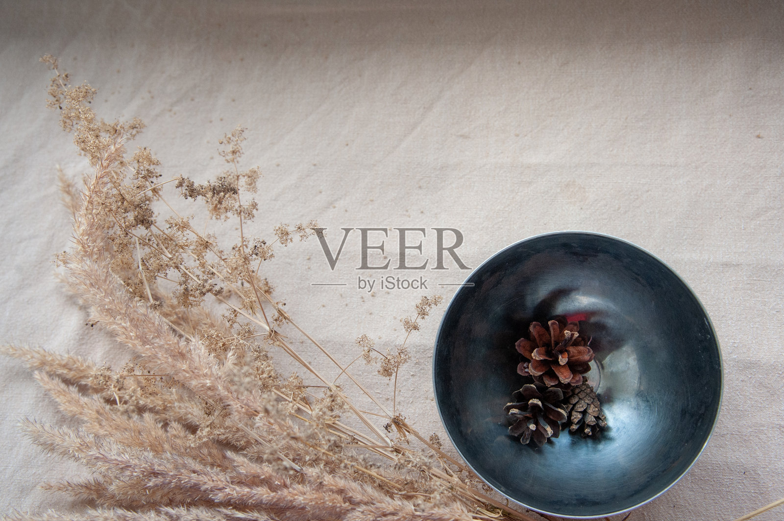 一个金属碗,上面有棕色的球果和干燥的植物。照片摄影图片