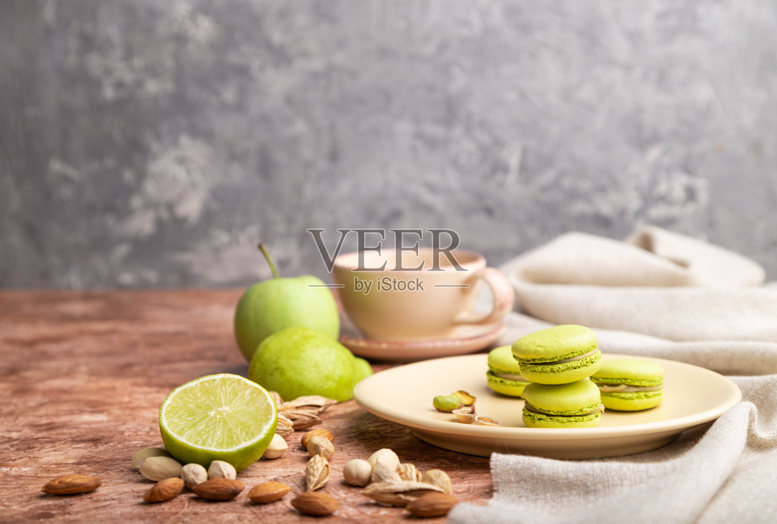 绿色的马卡龙或马卡龙蛋糕与一杯咖啡在棕色和灰色的混凝土背景和亚麻织物。侧视图,拷贝空间,选择性焦点。照片摄影图片