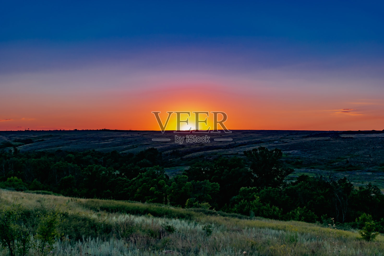 绿色植被覆盖的广阔田野上的彩色日落照片摄影图片