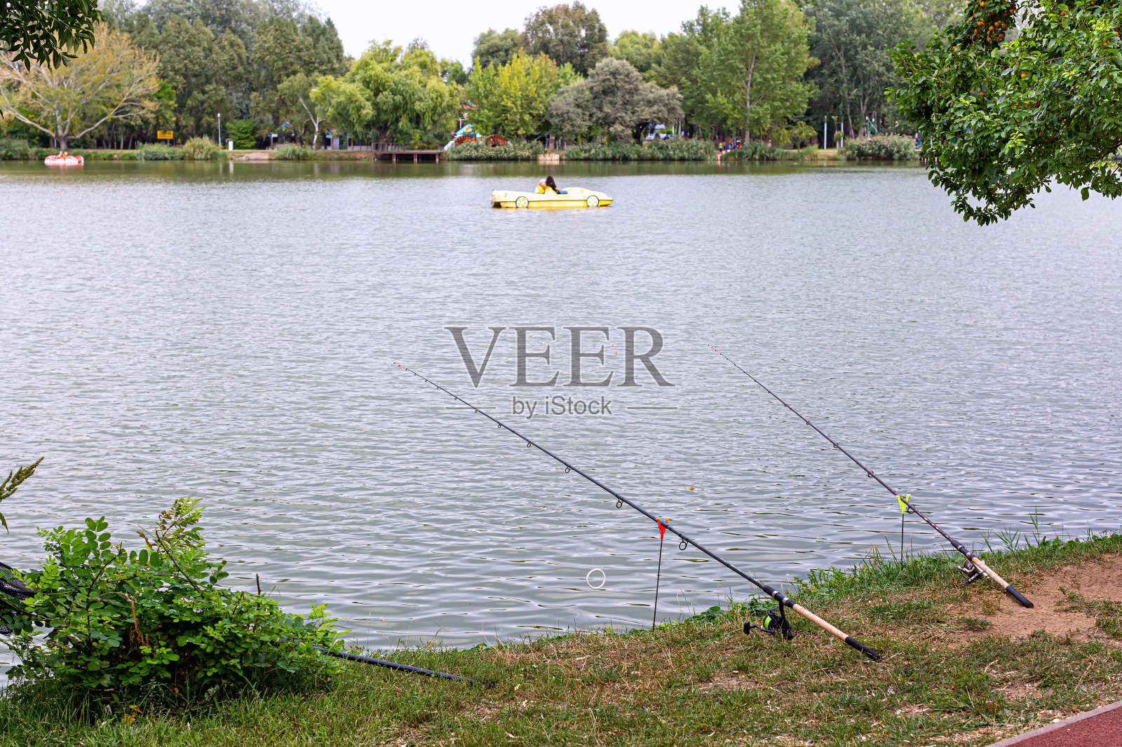 两根鱼竿安装在支架上,安装在湖边。美丽的湖景与黄色双体船照片摄影图片