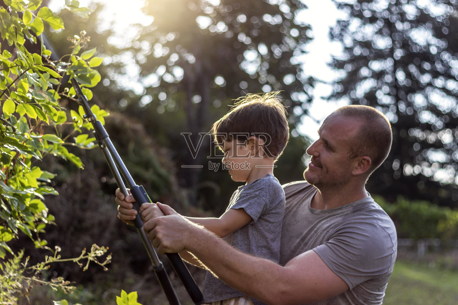 长着胡子的年轻父亲和他可爱的小儿子一起园艺。照片摄影图片