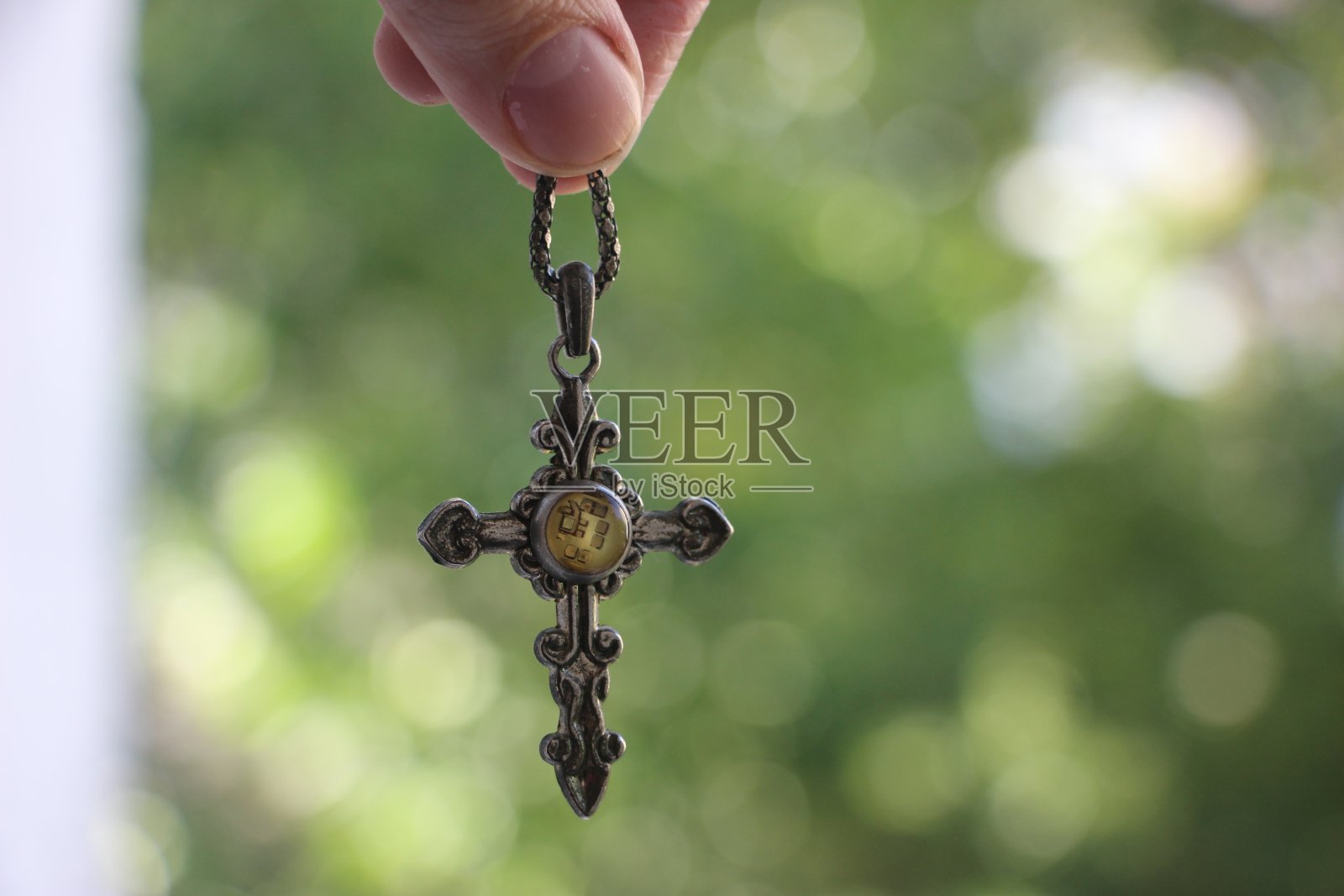 女人手握小银十字架与模糊的绿色自然背景照片摄影图片