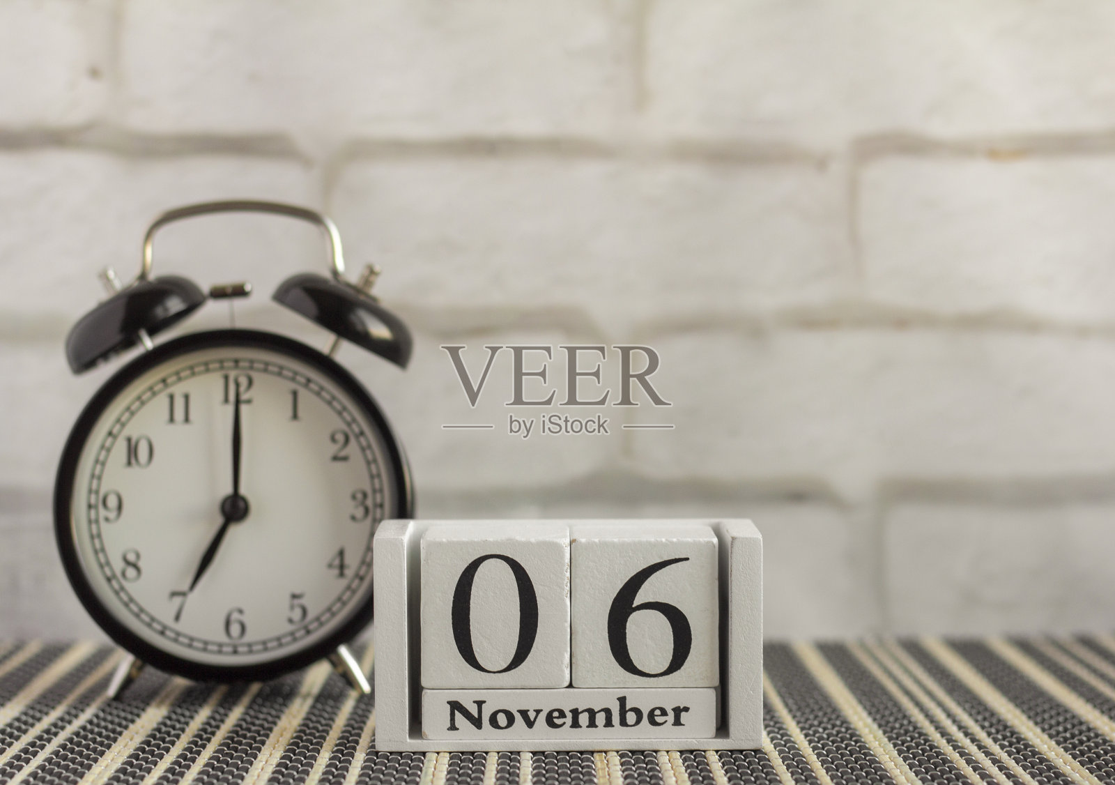 在一张黑色的桌子上,一个闹钟旁边的木制日历上写着11月6日。秋天的一天。11月份的日历。秋天照片摄影图片