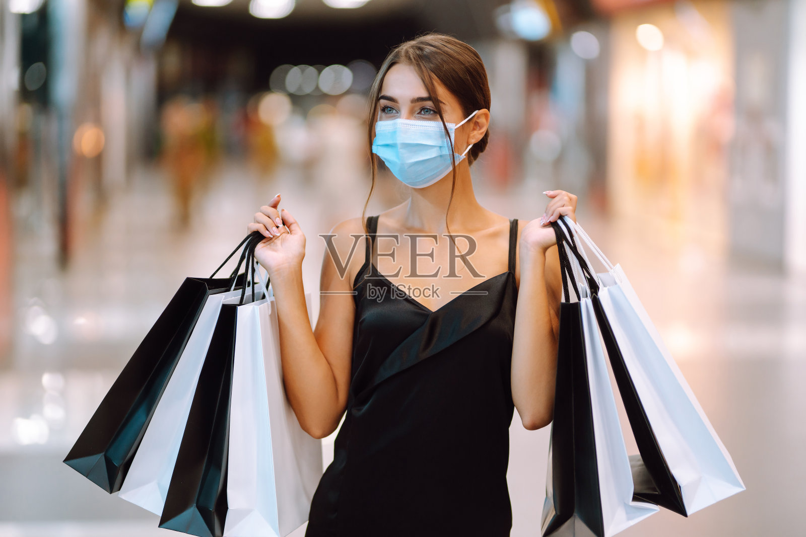 年轻女子在保护性消毒医疗口罩在她的脸与购物袋在商场。照片摄影图片