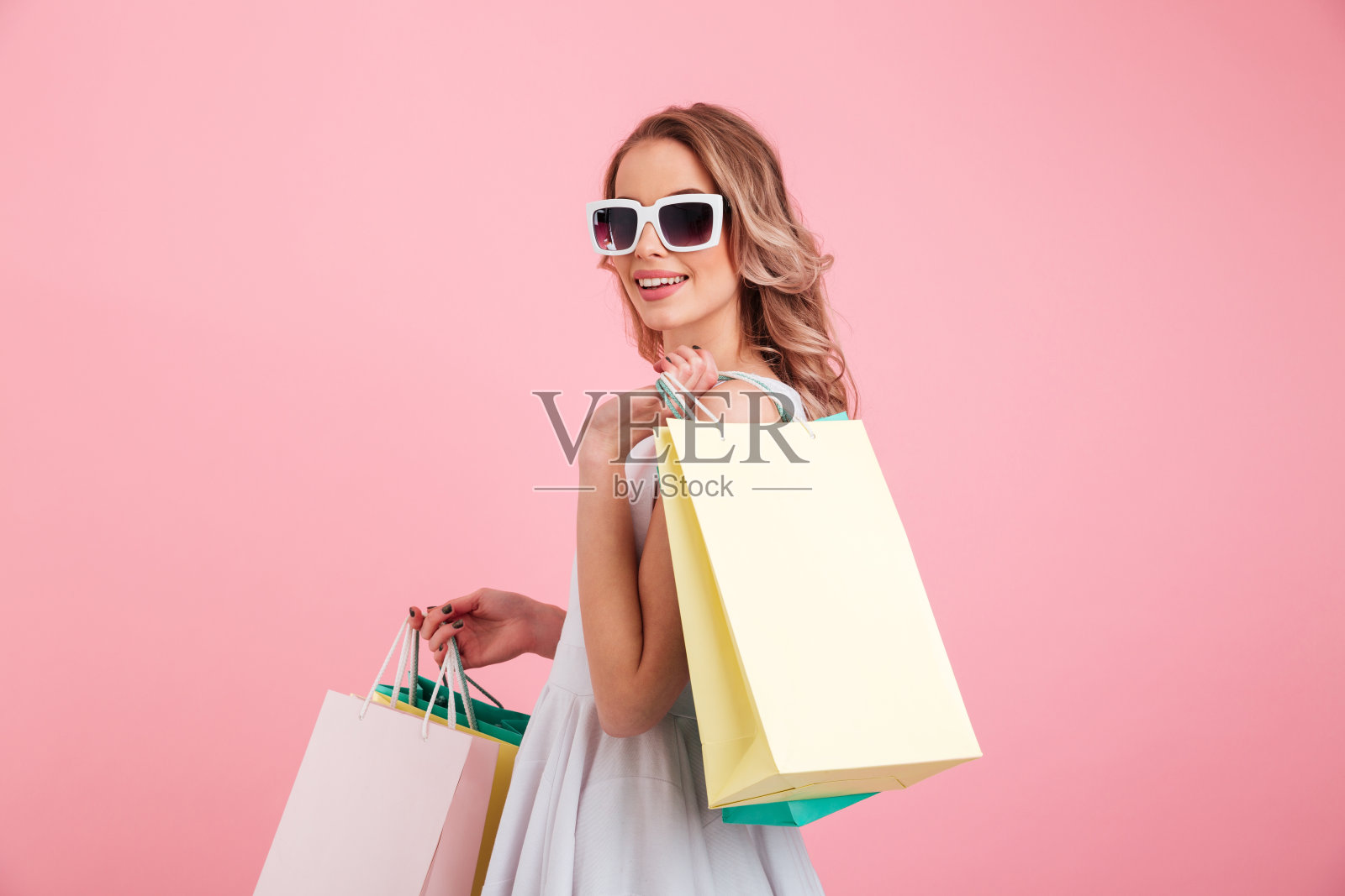 快乐的年轻女人戴着太阳镜拿着购物袋。照片摄影图片