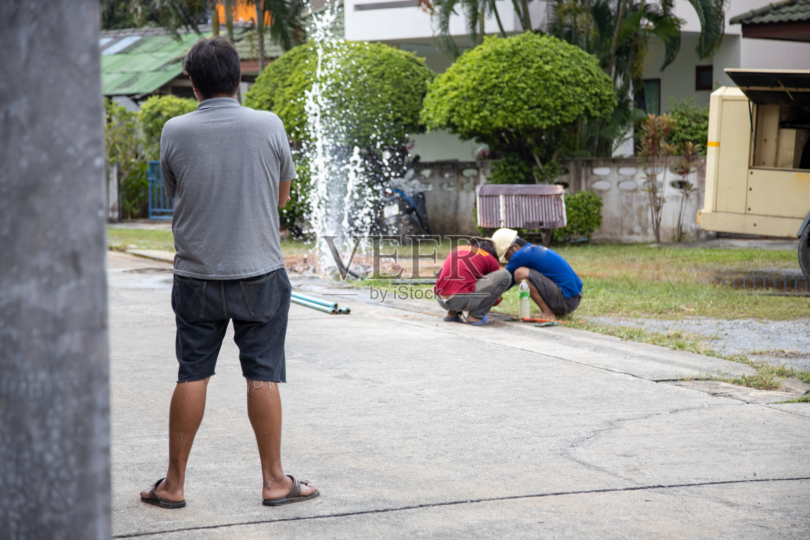 水管破裂。水正往喷泉里倒。公用事业工人拿着扳手,在沟渠中修理断裂的管子。照片摄影图片