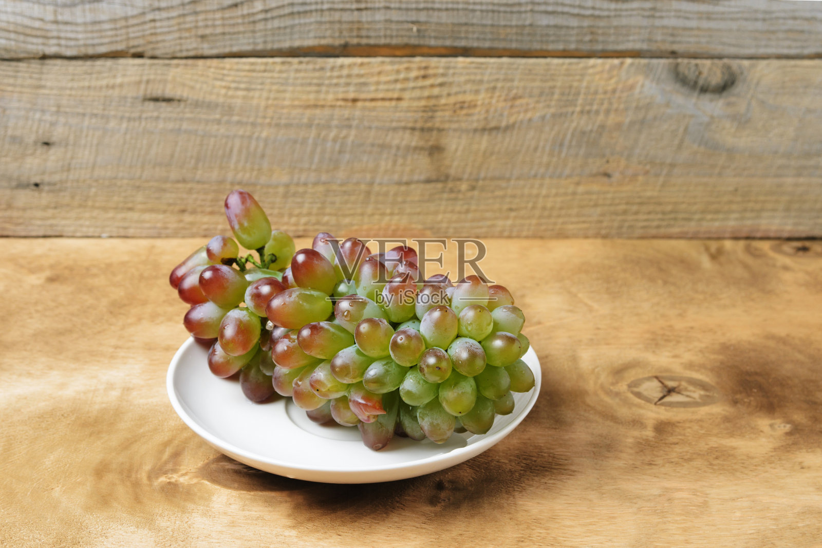 一串野葡萄在白色陶瓷盘在木背景。照片摄影图片