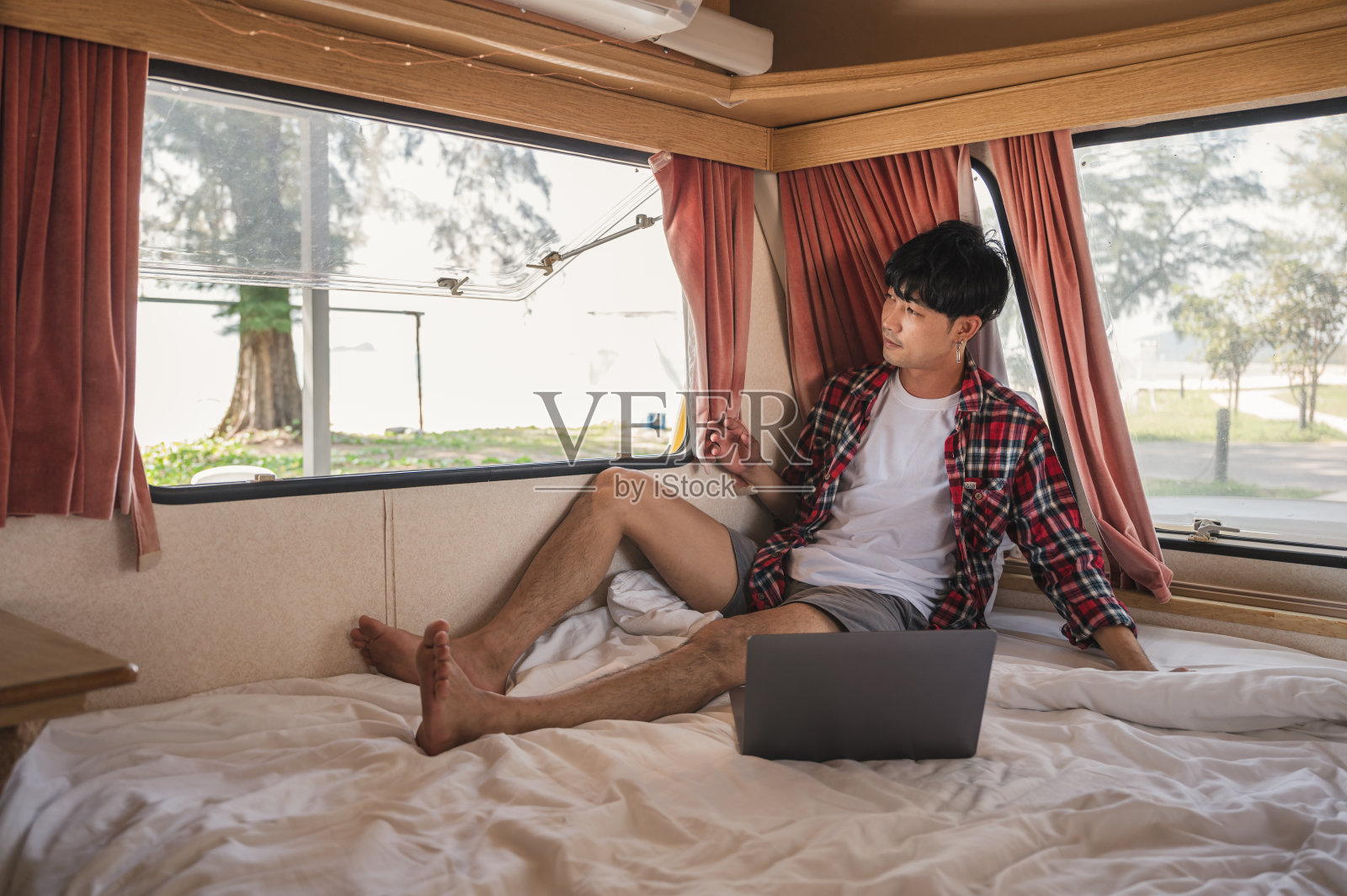 年轻的亚洲男子穿着斯科特衬衫放松与笔记本电脑在床上露营车照片摄影图片
